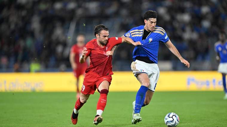 Kırmızı formalı oyuncu, mavi formalı rakibini geçmeye çalışırken futbol topu çim sahada ilerliyor.