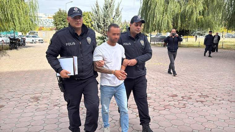 İki polis memuru, bir kişiyi kelepçeli olarak götürüyor.