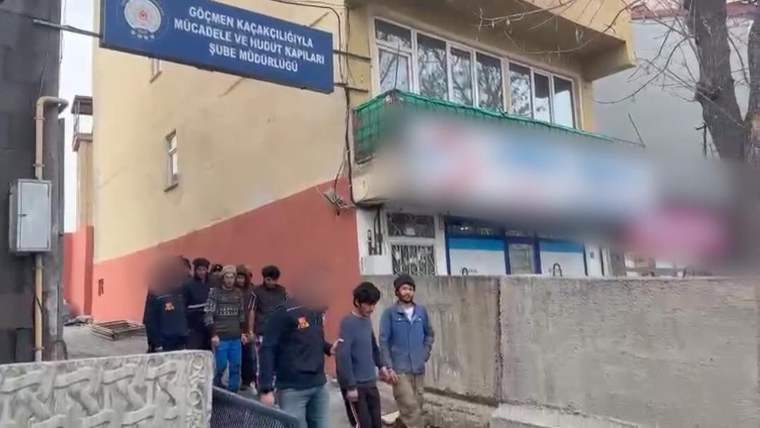 Göçmen kaçakçılığıyla mücadele şube müdürlüğü önünde bir grup insan yürüyor.
