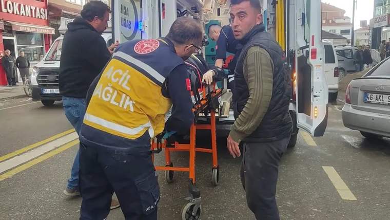 Sarı ve lacivert üniformalı iki sağlık görevlisi, sedyeyi ambulansın açık arka kapısına doğru taşıyor.