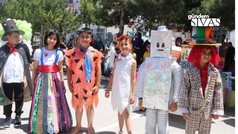 Atık malzemelerden yapılmış kostümler giymiş dört çocuk, bir etkinlikte poz veriyor.