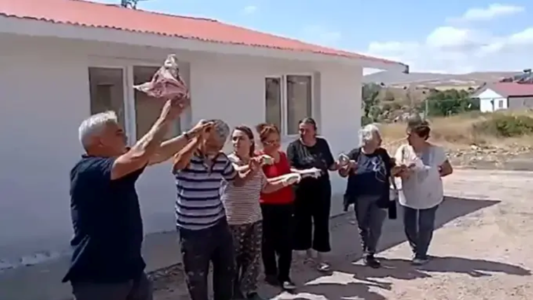 Bir grup yetişkin, beyaz bir binanın önünde ellerindeki nesneleri havaya kaldırarak yan yana duruyor.