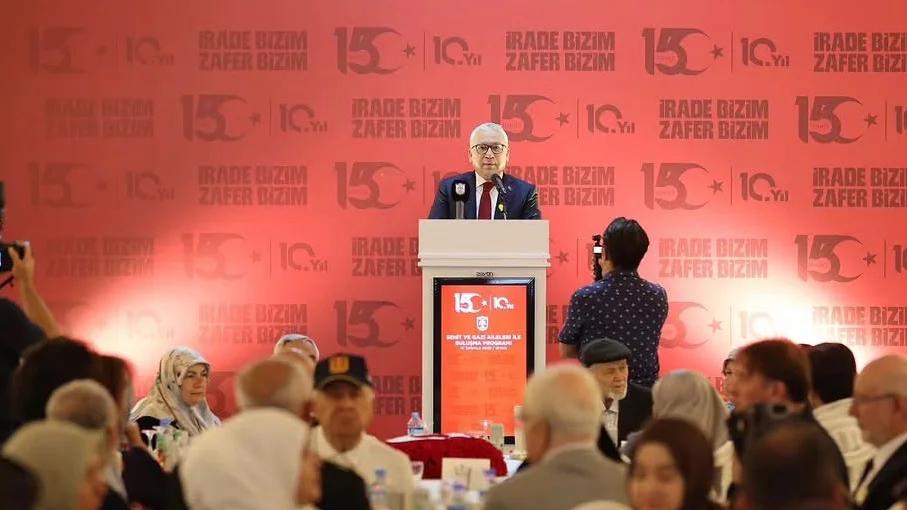 Kürsüde konuşan bir kişi, arka planda 'Rade Bizim Zafer Bizim' yazılı afişler var.