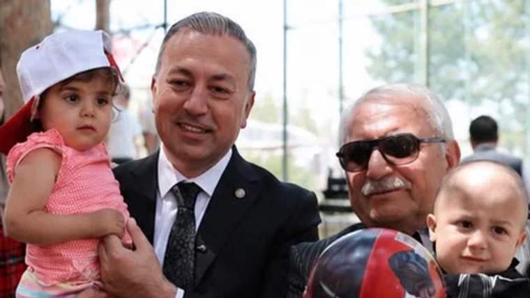 Takım elbiseli bir adam, kucağında çocukla; yanında güneş gözlüklü yaşlı adam ve iki çocuk görülüyor.