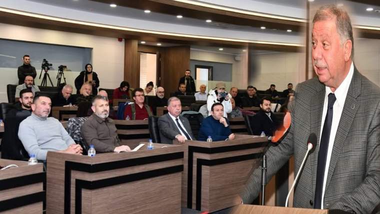 Kürsüde konuşan takım elbiseli bir kişi, toplantı salonunda oturan dinleyicilerin önünde görülüyor.