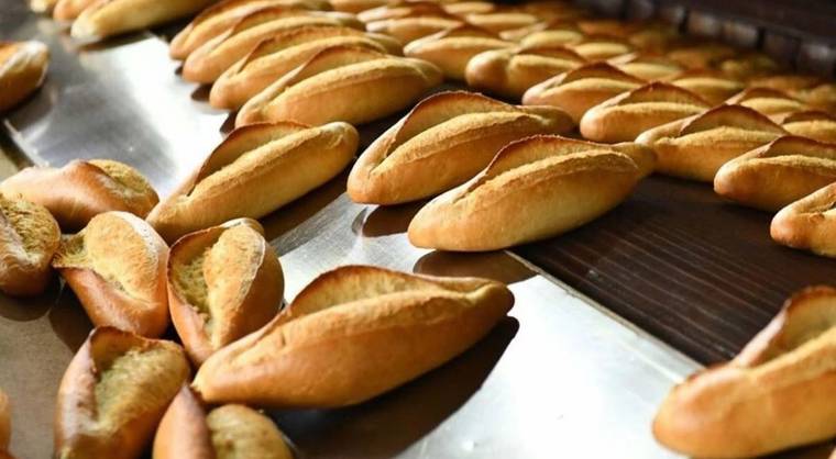 Metal tezgâh üzerinde farklı yönlere dizilmiş çok sayıda somun ekmek görülüyor.