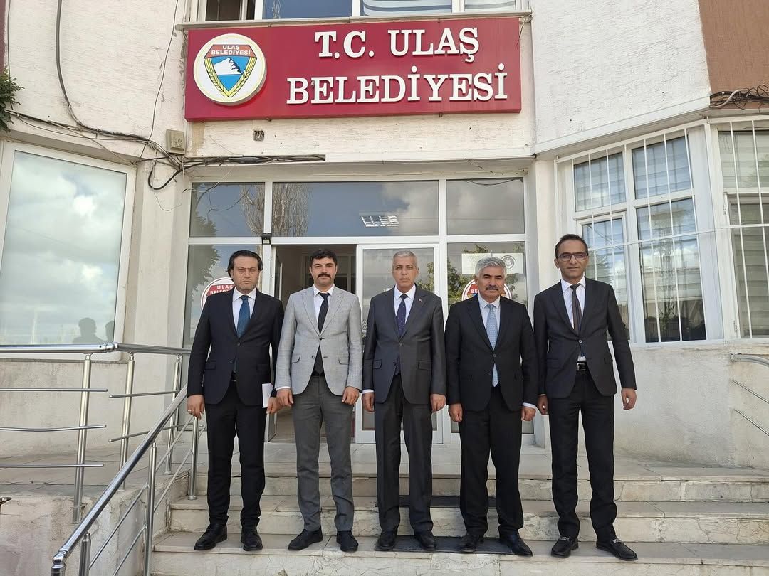 Belediye binası önünde beş kişi, resmi kıyafetlerle poz veriyor.