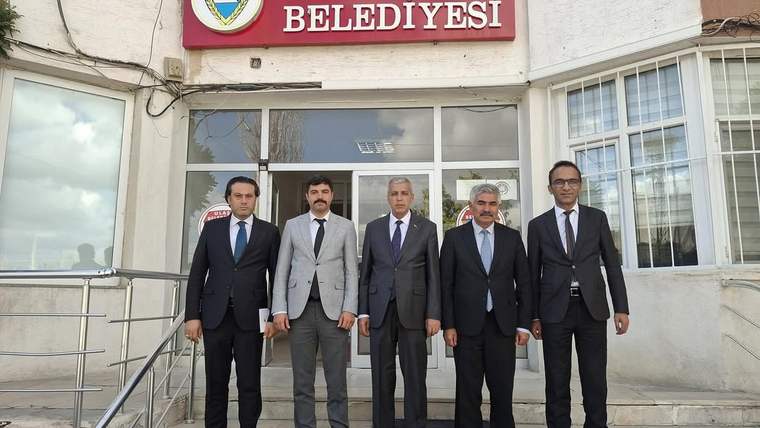 Belediye binası önünde beş kişi, resmi kıyafetlerle poz veriyor.