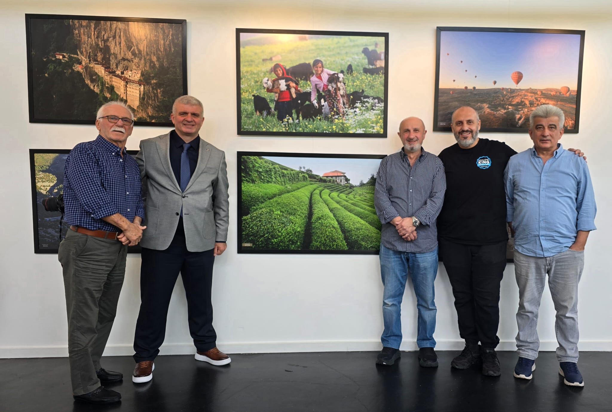 Sergi salonunda beş erkek, duvarlarda asılı doğa ve kültür temalı fotoğrafların önünde yan yana duruyor.