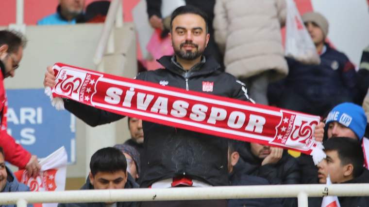 Sivasspor atkısı tutan bir taraftar, stadyumda coşkulu bir şekilde poz veriyor.