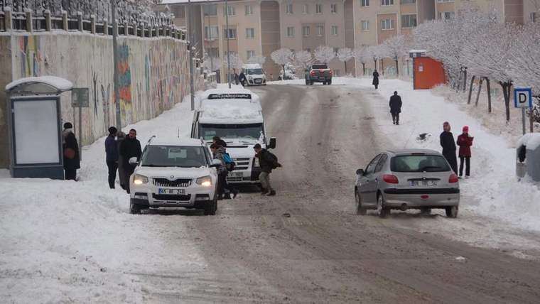 Kar yağışı sonrası karlı bir sokakta araçlar ilerlerken yayalar kaldırımda ve yol kenarında yürüyor.