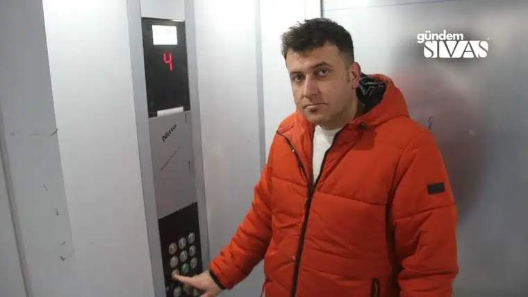 Turuncu montlu bir kişi, kat göstergesinde 4 yazan asansörde düğmelere basarken görülüyor.