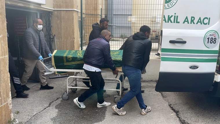 Bir grup insan, yeşil örtüyle kaplı bir tabutu hastane aracına taşıyor.