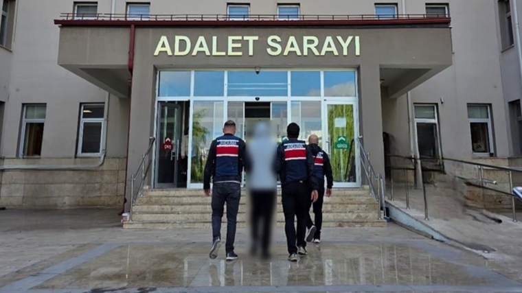 “Adalet Sarayı” yazılı binanın girişinde üç üniformalı görevli, yüzü bulanıklaştırılmış bir kişiyi yürütüyor.