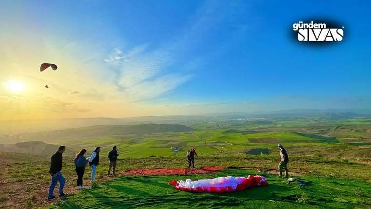 Yamaç paraşütü yapan kişiler, yeşil bir alanda hazırlık yapıyor.