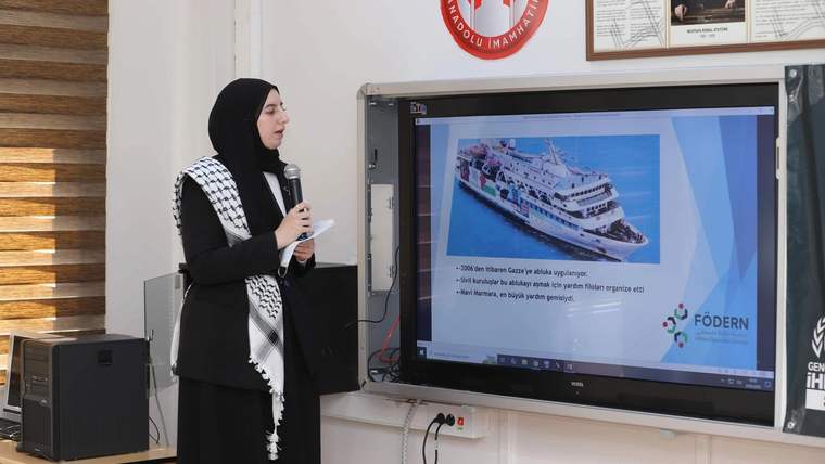 Kareli bir örtü giymiş bir kadın, projeksiyon cihazında bir geminin fotoğrafını gösteriyor.