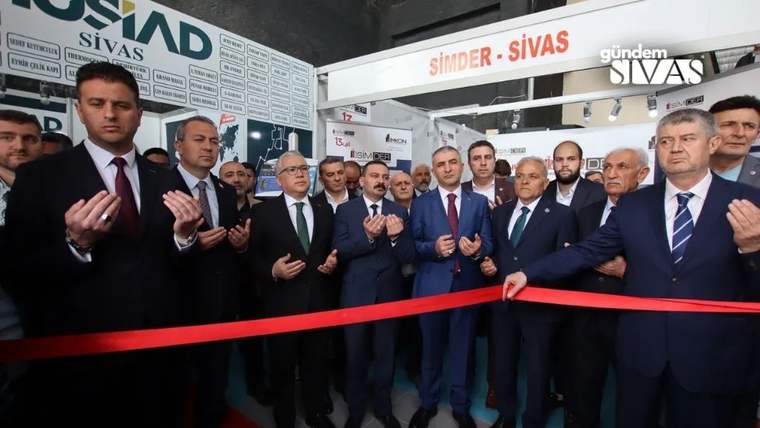 SİMDER-SİVAS yazılı pano önünde, kırmızı kurdelenin arkasında takım elbiseli bir grup erkek duruyor.