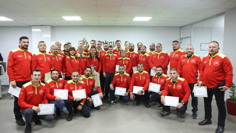 Kırmızı mont giymiş bir grup insan, sertifikalarını tutarak poz veriyor.