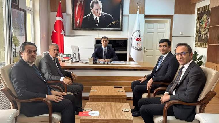 Ofis ortamında, masanın etrafında oturan dört kişi ve duvarda Atatürk portresi.