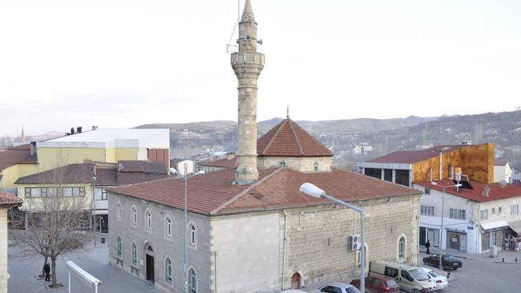Gürün Ulu Camii, taş yapısı ve minaresiyle birlikte görünmekte, çevresinde binalar ve park halindeki araçlar var.