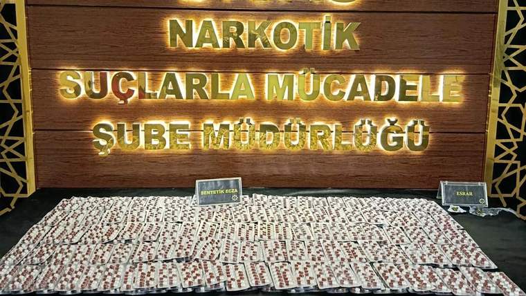Narkotik suçlarla mücadele şube müdürlüğü tabelası önünde, üzerinde haplar bulunan paketler yer alıyor.
