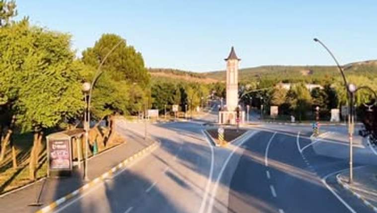 Sivas Cumhuriyet Üniversitesi kampüsüne giden geniş bir yol, yol kenarında ağaçlar ve bir saat kulesi görünmekte.