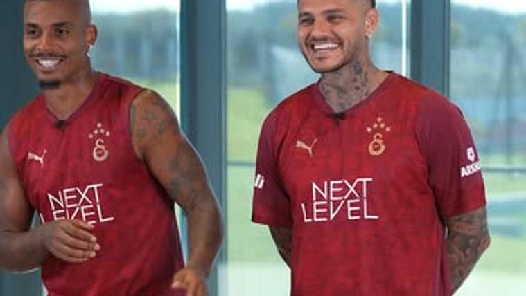 Kırmızı formalı iki futbolcu, geniş pencereli bir salonda yan yana duruyor; altta forma çizimi var.