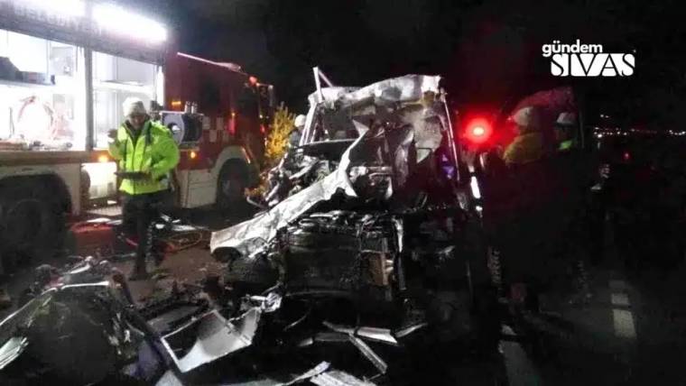 Gece çekiminde ağır hasarlı bir araç, yanında itfaiye aracı ve reflektif giysili kişiler görülüyor.