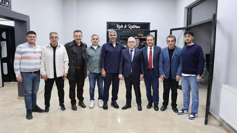 Bir binanın koridorunda dokuz erkek, duvarlardaki kapı ve tabelaların önünde yan yana duruyor.