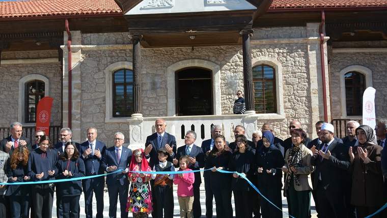 Taş cepheli tarihi bina önünde, kurdele tutan yetişkinler ve çocuklardan oluşan kalabalık bekliyor.