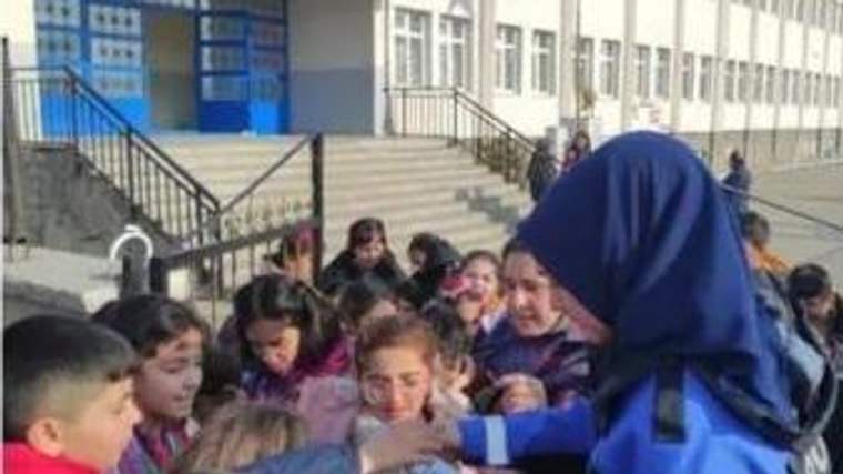 Melikşah İlkokulu önünde mavi kıyafetli bir kadın, çevresindeki öğrencilerle konuşuyor.