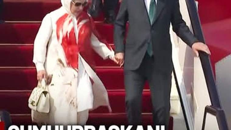 Kırmızı halı kaplı merdivenlerden inen takım elbiseli bir erkek ile beyaz giyimli, başörtülü bir kadın el ele.