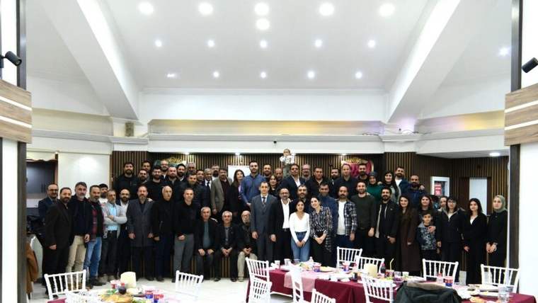Salon içinde uzun masaların önünde, çoğu takım elbiseli kalabalık bir grup birlikte poz veriyor.