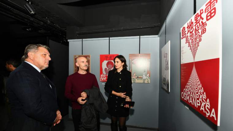 Üç kişi, duvarda asılı Türk-Japon dostluğunu simgeleyen posterleri inceliyor.