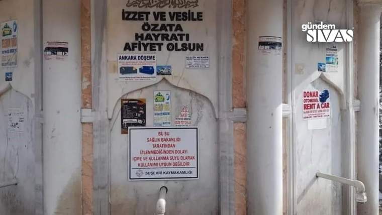 Duvar üzerindeki hayrat ve su uyarısı yazılarıyla birlikte, ortada bir çeşme musluğu görülüyor.