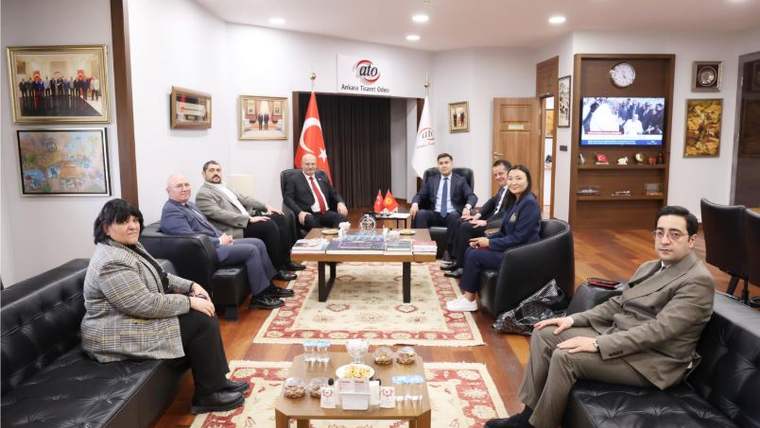 Bir odada koltuklara oturan kalabalık bir grup, ortadaki sehpanın çevresinde birlikte poz veriyor.