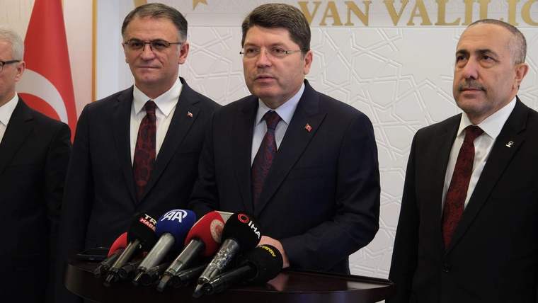 Üç kişi, masanın arkasında mikrofonların önünde duruyor. Arkada Türk bayrağı ve Van Valiliği logosu var.