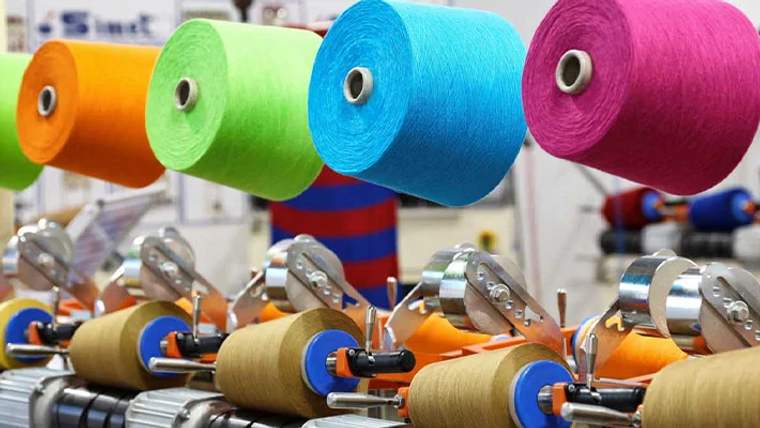 Turuncu, yeşil, mavi ve pembe iplik makaraları, tekstil makinelerinin metal parçaları üzerinde duruyor.