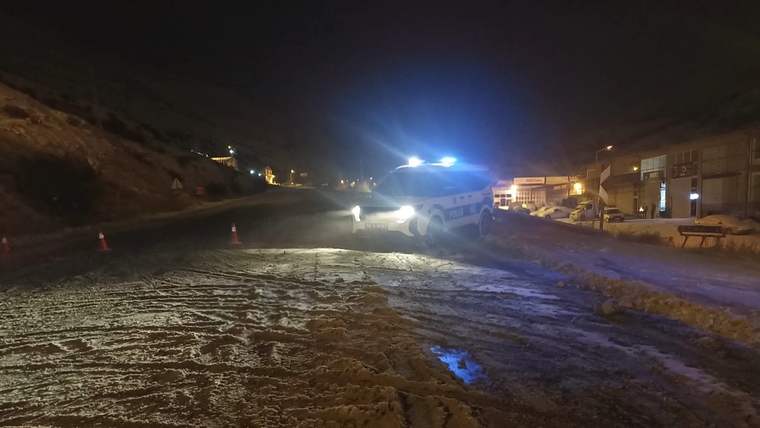 Karla kaplı yolda, yanlarında uyarı koni bulunan bir polis aracı duruyor.