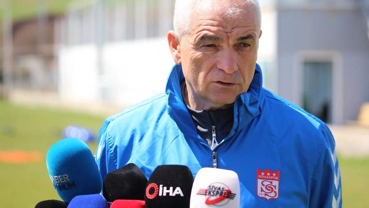 Mavi spor montlu bir kişi, açık havada farklı kurumlara ait mikrofonlara konuşuyor.