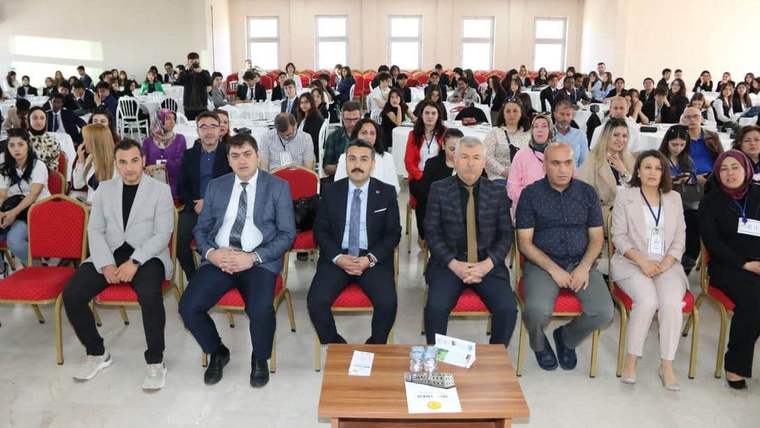 Bir salonda sıralar halinde oturan kalabalık, ön sırada yedi kişi ve önlerinde üzerinde belgeler bulunan masa.