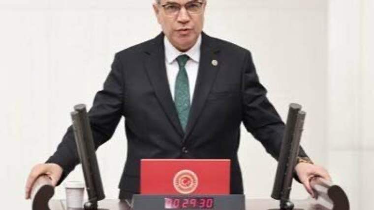 Kürsüde duran takım elbiseli bir kişi, iki mikrofon arasında Meclis konuşma ekranının önünde görülüyor.