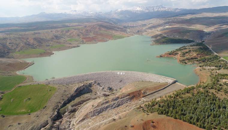Yeşil suyla kaplı bir baraj gölü ve çevresindeki dağlık alanlar, uzaktan görünüm.