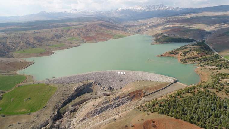 Yeşil suyla kaplı bir baraj gölü ve çevresindeki dağlık alanlar, uzaktan görünüm.