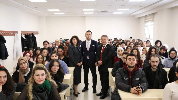 Bir sınıfta, genç iletişimcilerle birlikte duran üç kişi ve oturan öğrenciler. Sınıf düzenli ve aydınlık.