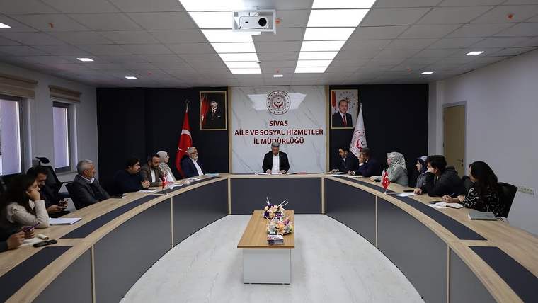 Sivas Aile ve Sosyal Hizmetler İl Müdürlüğü yazılı salonda, uzun masanın çevresinde toplantı yapan kişiler