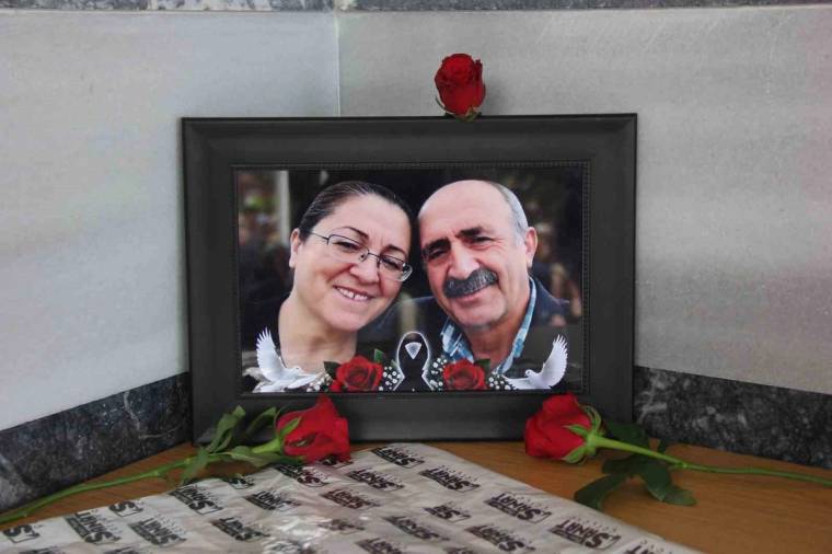 Siyah çerçeveli portre fotoğrafının önünde kırmızı güller ve üzerinde yazılar bulunan örtü yer alıyor.