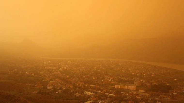 Hava, çöl tozu nedeniyle sarımsı bir renge bürünmüş, şehir manzarası bulanık görünüyor.