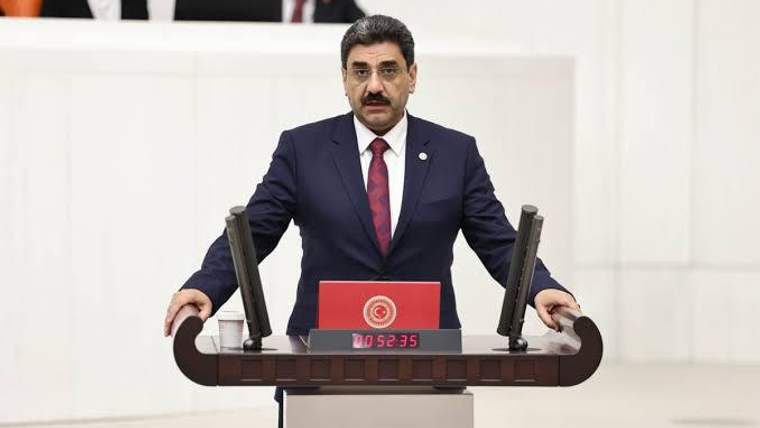 Kürsüde konuşan bir kişi, arka planda milletvekilleri yer alıyor.
