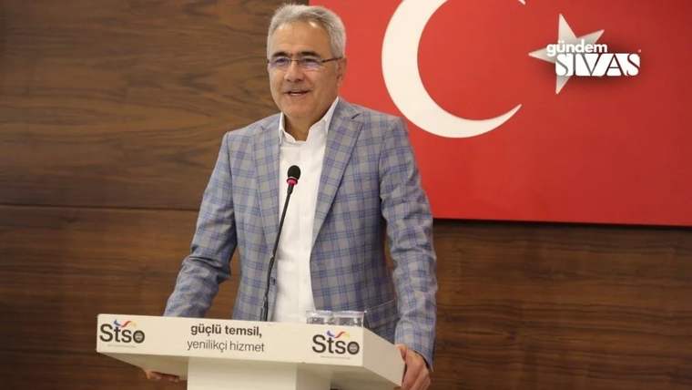 Mavi kareli ceket giymiş bir kişi, kürsüde konuşma yapıyor.